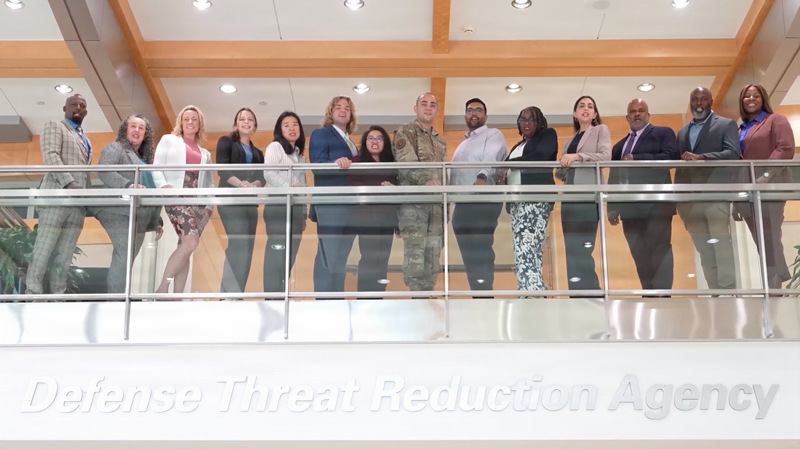 DTRA employees on balcony with the words Defense Threat Reduction Agency below.